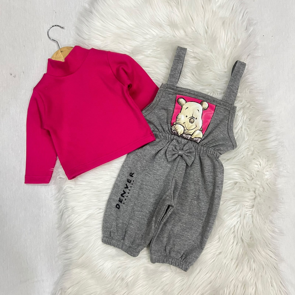 Vibrant hot pink ribbed turtleneck layered under heather grey Winnie the Pooh overalls. Features a charming central bow, elasticated cuffs, and a cute "Denver" print detail fleece stuff