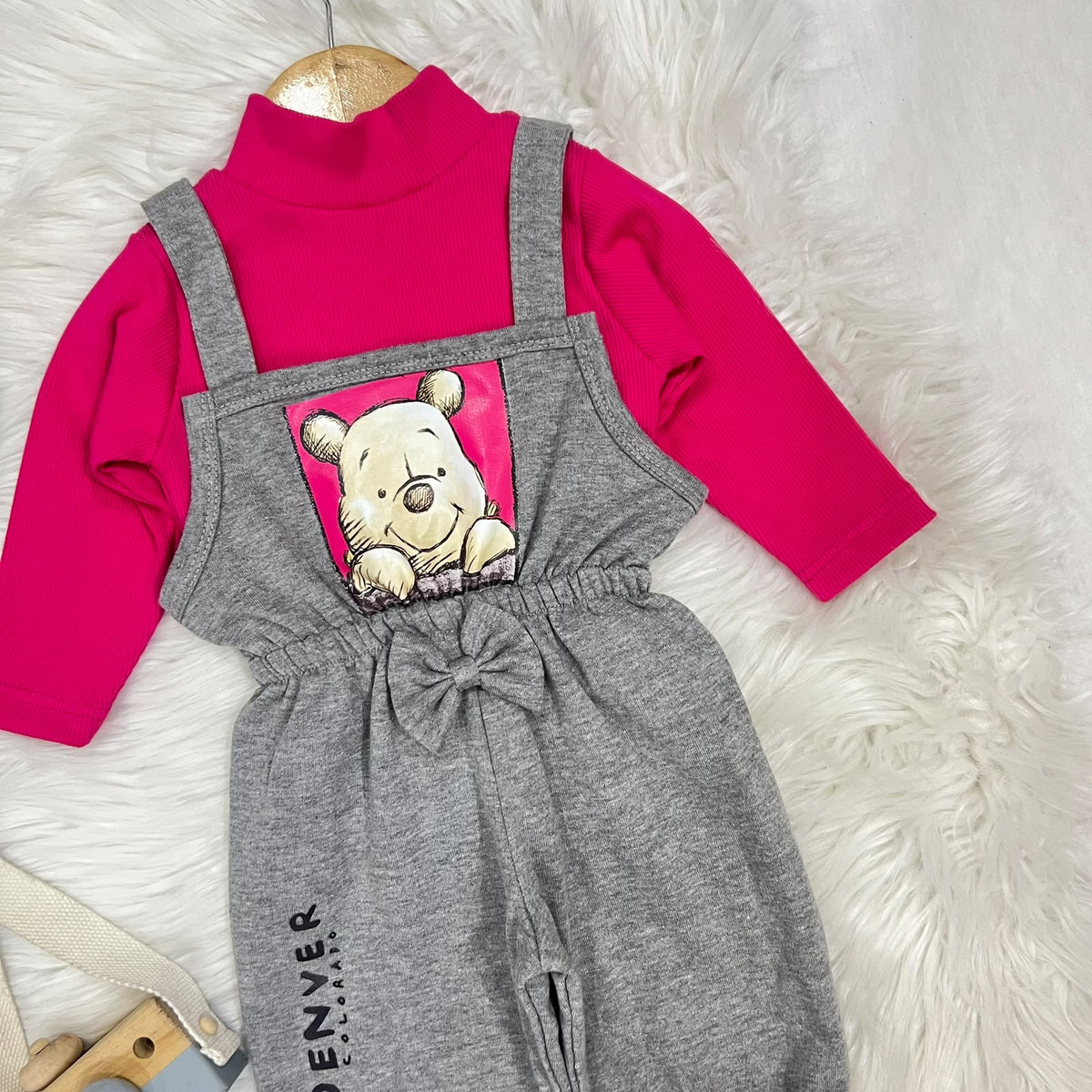 Vibrant hot pink ribbed turtleneck layered under heather grey Winnie the Pooh overalls. Features a charming central bow, elasticated cuffs, and a cute "Denver" print detail fleece stuff