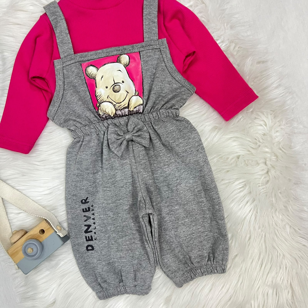 Vibrant hot pink ribbed turtleneck layered under heather grey Winnie the Pooh overalls. Features a charming central bow, elasticated cuffs, and a cute "Denver" print detail fleece stuff