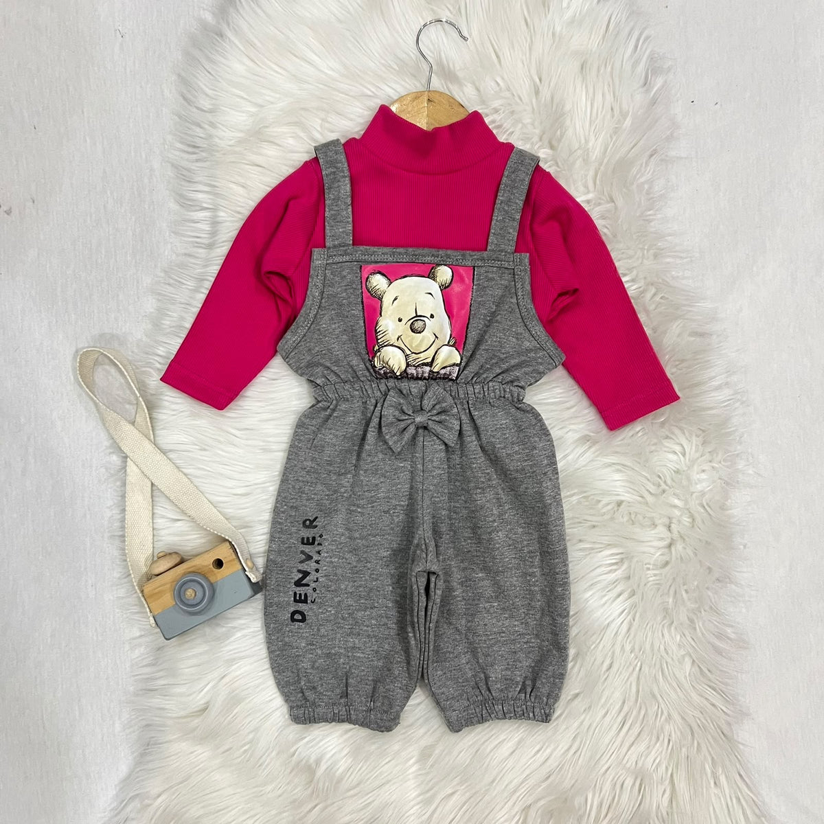 Vibrant hot pink ribbed turtleneck layered under heather grey Winnie the Pooh overalls. Features a charming central bow, elasticated cuffs, and a cute "Denver" print detail fleece stuff